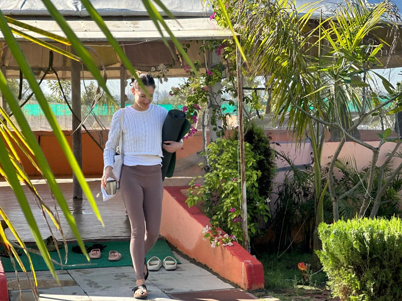 A yoga student walking along a garden path with her yoga mat on the way to class