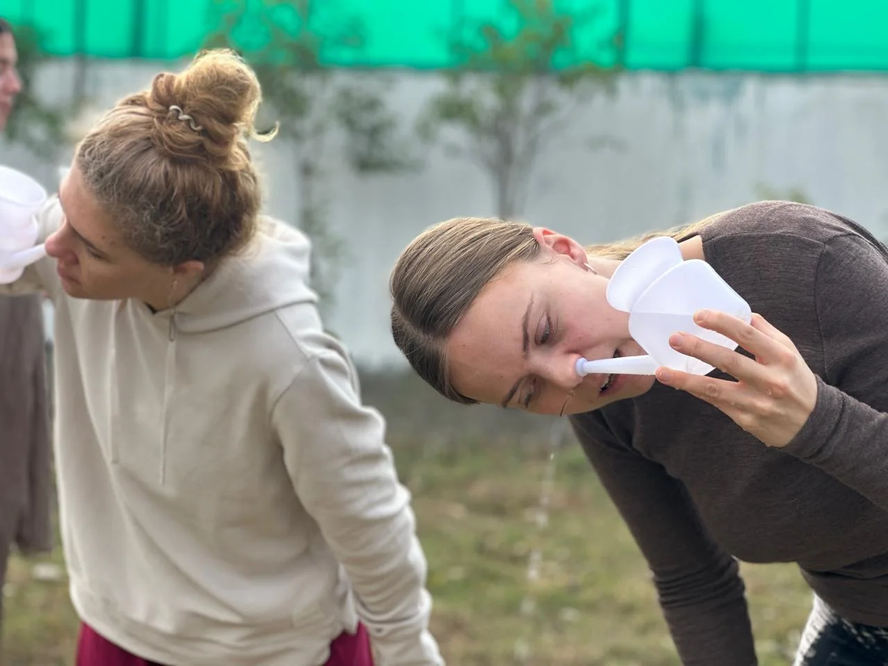 Two students practising Jala Neti nasal cleansing with neti pots outdoors at a yoga school in Rishikesh