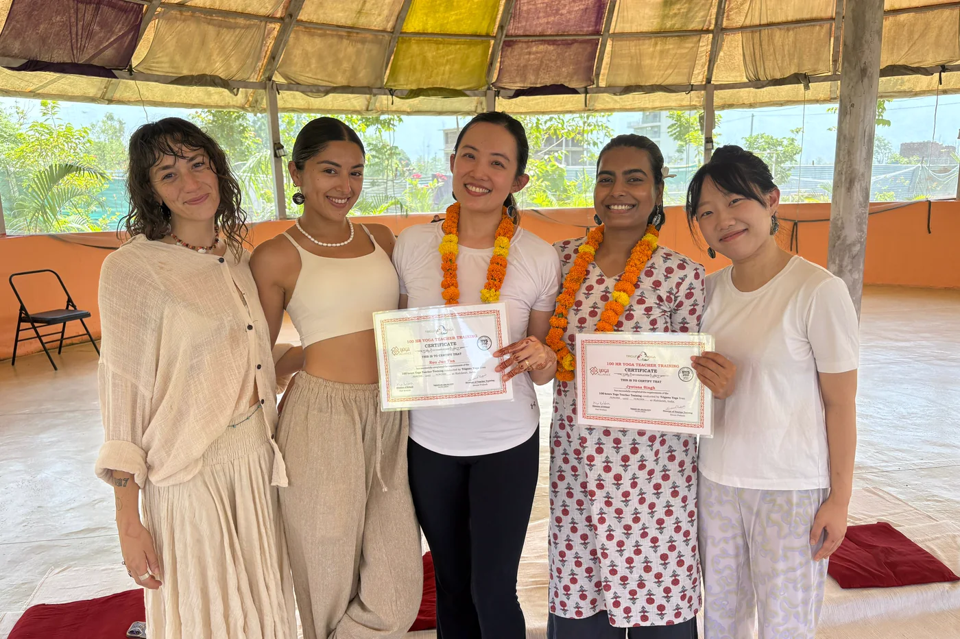 Graduates holding certificates in the dome hall at Triguna Yoga School, which runs 100 hour and 200 hour yoga teacher training