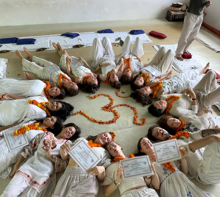 Graduates with their Yoga Alliance course certificates around a marigold Om at Triguna Yoga School
